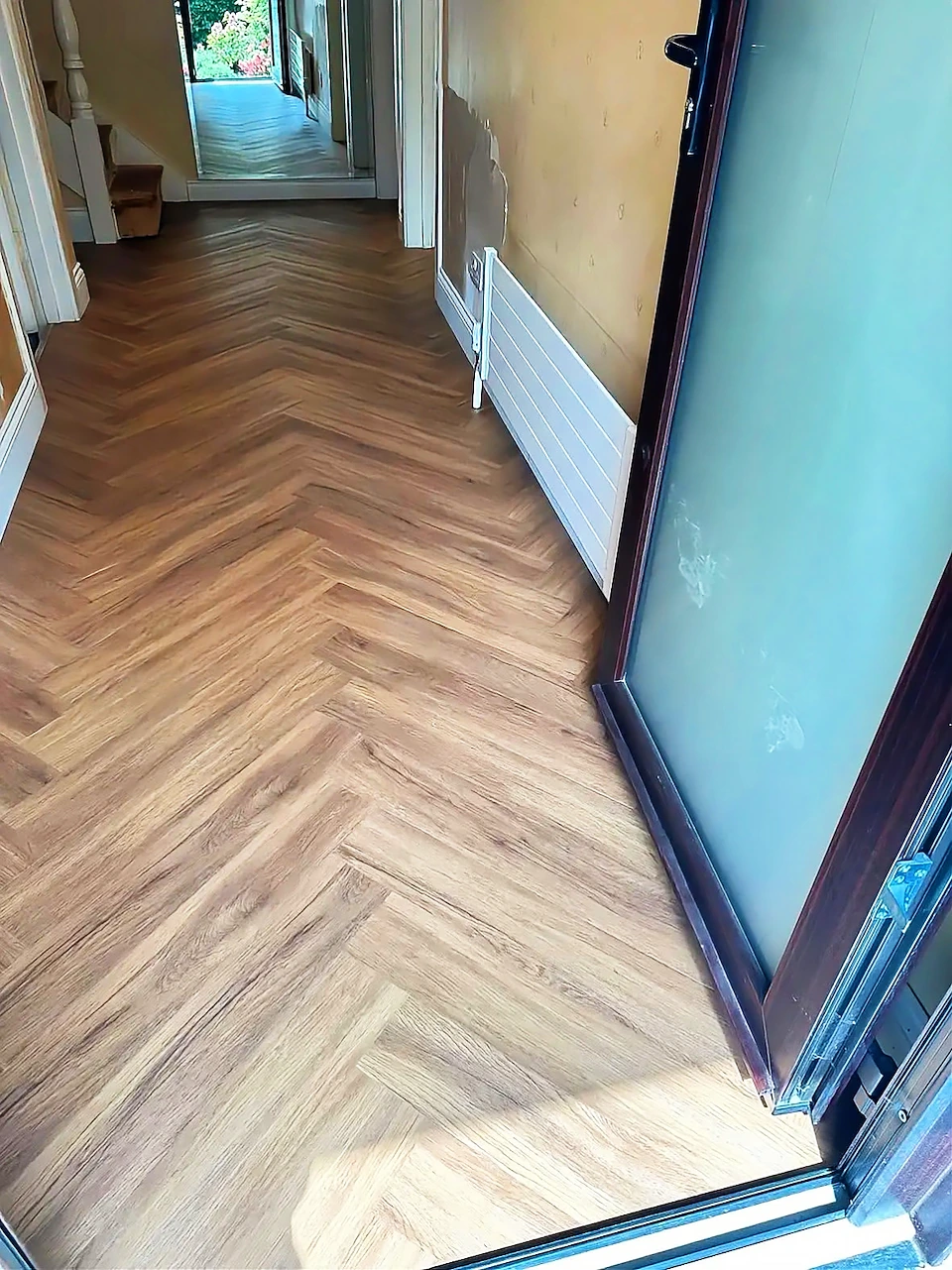 Herringbone oak-effect flooring fitted through a bright hallway