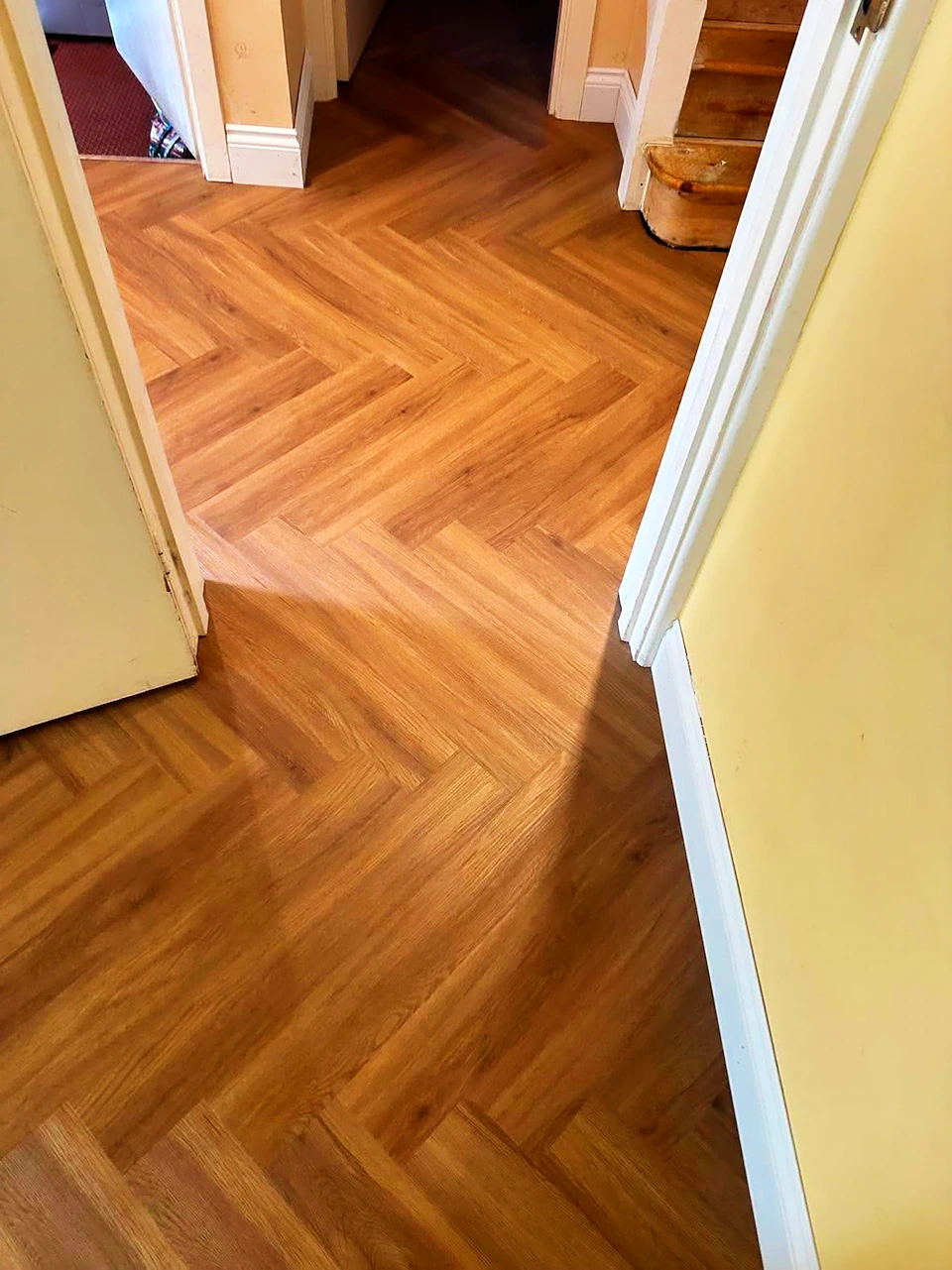 Honey oak herringbone LVT fitted through a hallway and continuing into the next room