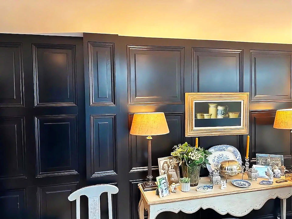 Finished black wall panelling in a living room with an antique console table and lamps